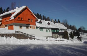 Gasthaus Feistritzsattel, © Tourismusbüro Kirchberg/Wechsel Verschneites Gasthaus mit Holzfassade und blauen Himmel im Hintergrund.
