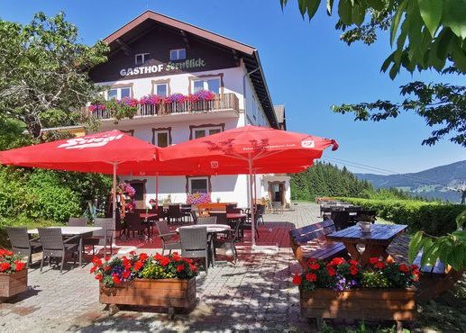 Alpengasthof Fernblick, Fam. Pölzelbauer, © Alpengasthof Fernblick, Fam. Pölzelbauer Ein traditioneller Gasthof mit Terrasse, roten Sonnenschirmen und Blumenkästen vor einem klaren blauen Himmel.