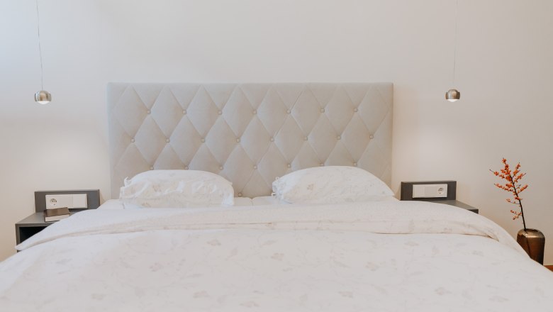 Nächtigen im Löffler, © Der Löffler - Nicole Seiser Ein elegantes Schlafzimmer mit einem großen Bett, zwei Nachttischen und einer Vase mit roten Beeren.