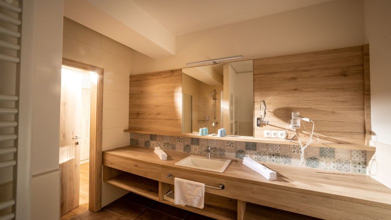 Hotel Mönichwalderhof, © Tourismusverband Oststeiermark, Karl Schrotter Modernes Badezimmer mit Holzverkleidung, Waschbecken, Spiegel und Handtüchern.