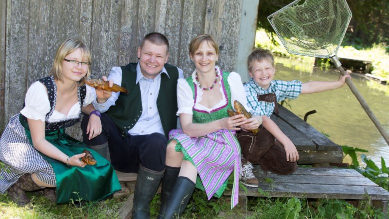 Forellengasthof Joglland, © Harry Schiffer Eine Familie in Tracht sitzt lachend vor einem Teich.