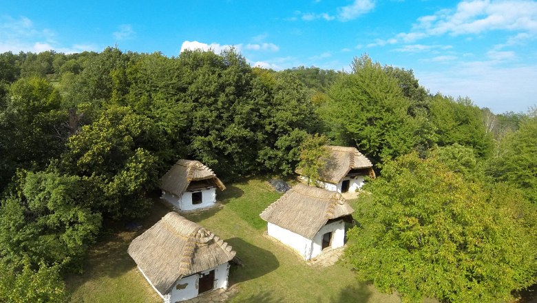 Kellerreihe von Cák, © Cáki pincesor Luftaufnahme von traditionellen, strohgedeckten Hütten in einer grünen Landschaft.