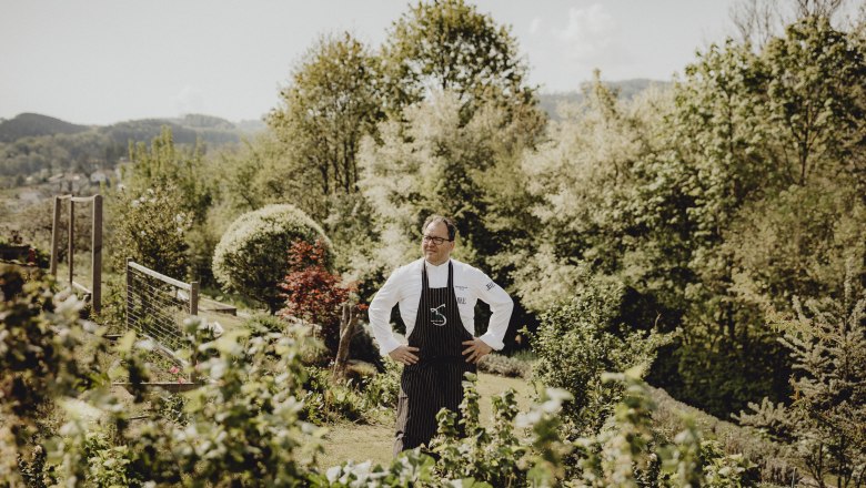 Haubenkoch Uwe Machreich, © Niederösterreich Werbung/Sophie Menegaldo Ein Koch steht in einem Garten mit Bäumen im Hintergrund.