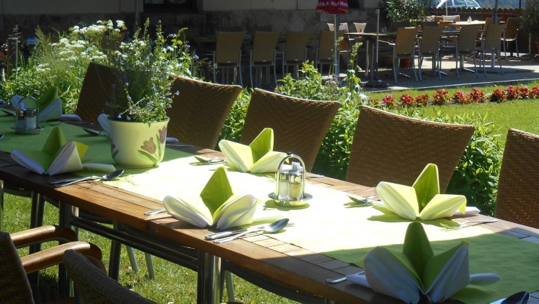 Im Sommer im Garten speisen, © Hotel Belvedere Gedeckter Tisch im Garten mit grünen Servietten und Blumen.