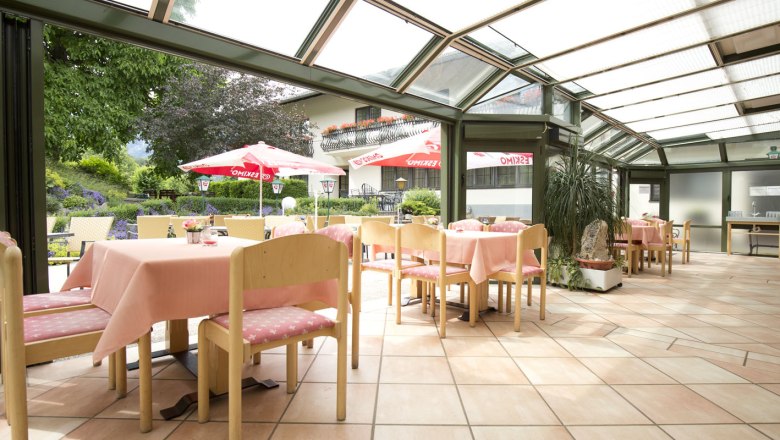 Restaurant, © Gasthof Flackl Helles Restaurant mit Glasdach, rosa Tischdecken und Blick auf Garten mit Sonnenschirmen.