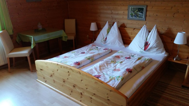 Szobák a Wachabauer farmon, © Wachabauer Hangulatos szoba fából készült falakkal, franciaággyal és asztallal a Wachabauer farmon.