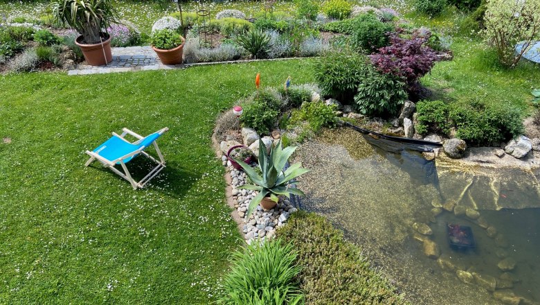 Blick vom Balkon, © Wiener Alpen Garten mit Liegestuhl, Teich und Pflanzen.