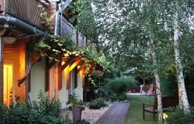 Köszeghegyalja Vendégház, © Kőszeghegyalja Vendégház Gartenansicht eines Gästehauses mit beleuchteter Terrasse und Bäumen.