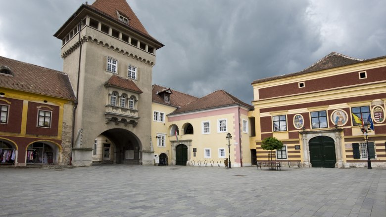 Heldentor, © Hősök tornya Historischer Platz mit alten Gebäuden und einem Turm unter bewölktem Himmel.