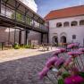vierzigerhof, © Niederösterreich Werbung / Maximilian Pawlikowsky Ein Innenhof mit Kopfsteinpflaster, Tischen und Stühlen, umgeben von Gebäuden mit Arkaden und einem modernen Balkon.