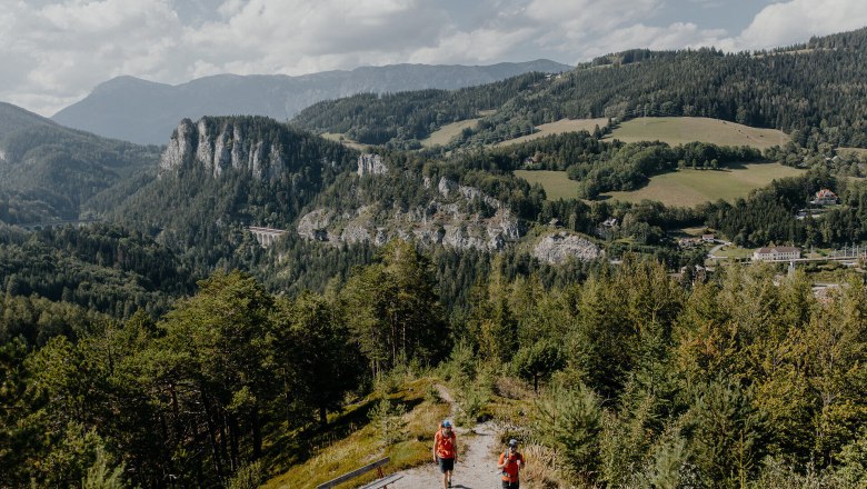 Semmering Bahnwanderweg, Bahnwandern, Wiener Alpen in Niederösterreich, © Wiener Alpen/nicoleseiser.at Blick auf die Pollereswand mit Viadukt, dem 20 Schilling Blick, Davor sind zwei Wanderer zu sehen.
