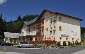 Roseggerhof, © Roseggerhof, Steindl Ein großes, traditionelles Gebäude mit Holzverzierungen und Blumenkästen, umgeben von Bäumen und einem Parkplatz.