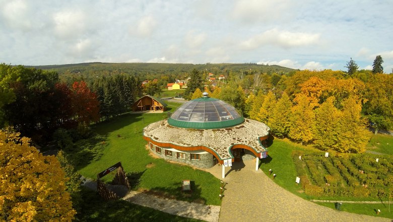 Besucherzentrum, © Bechtold Luftaufnahme eines runden Gebäudes mit Glaskuppel, umgeben von herbstlichen Bäumen und einem Garten.