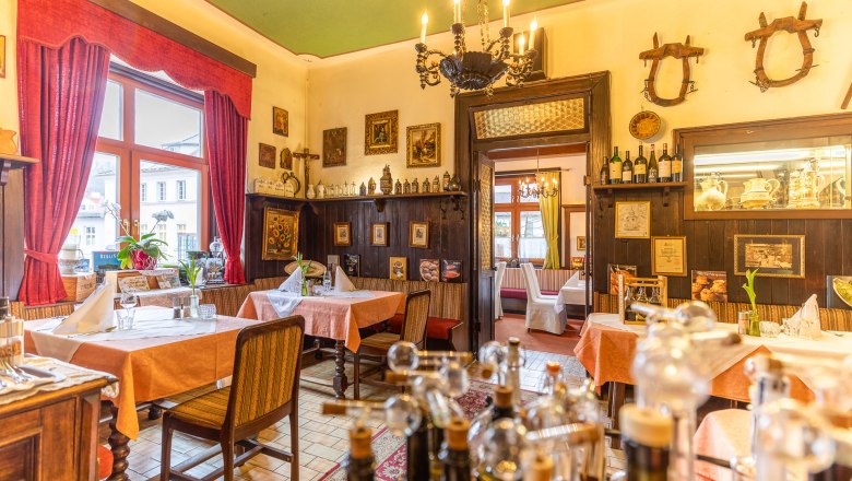 Stüberl, © Christian Krems Gemütliches Restaurant mit Holzmöbeln, roten Vorhängen und dekorativen Bildern an den Wänden.