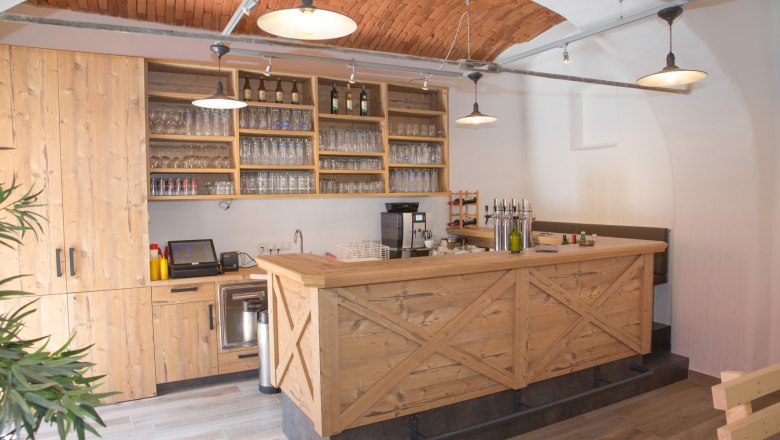 Szalon, © Christian Piribauer Fa bárpult poharakkal és palackokkal, tégla mennyezet.