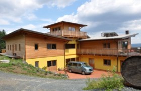 Kögl-Hof, © Gregor Kögl Ein modernes, zweistöckiges Gebäude mit Holzverkleidung und gelber Fassade, umgeben von Natur.