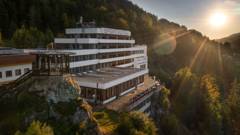 Sporthotel Sonnenuntergang, © Sporthotel Semmering Ein Hotel auf einem Hügel bei Sonnenuntergang, umgeben von Wald.