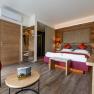 Das Gästehaus im Triad, © Marketing Platzhirsch, Gobauer Modernes Gästezimmer mit Doppelbett, Holzmöbeln und roten Akzenten.