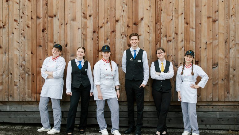 Tourismusschule Semmering, © Wiener Alpen/Sophie Menegaldo Sechs junge Menschen in Uniformen vor einer Holzwand.