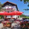 Alpengasthof Fernblick, Fam. Pölzelbauer, © Alpengasthof Fernblick, Fam. Pölzelbauer Ein traditioneller Gasthof mit Terrasse, roten Sonnenschirmen und Blumenkästen vor einem klaren blauen Himmel.