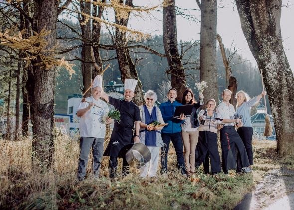 Berghof-Team, © Gasthof Berghof Eine Gruppe von Menschen in Kochkleidung steht fröhlich in einem Wald.