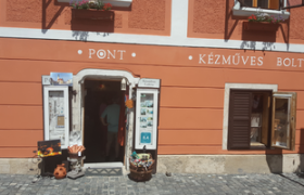 Pont-Vendeghaz, © Pont-Vendeghaz Eingang eines Handwerksladens mit orangefarbener Fassade und Blumenkästen.