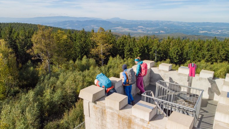 Wanderung über den Geschriebenstein, © Wiener Alpen, Martin Fülöp Drei Wanderer auf einem Aussichtsturm mit Blick auf bewaldete Hügel.