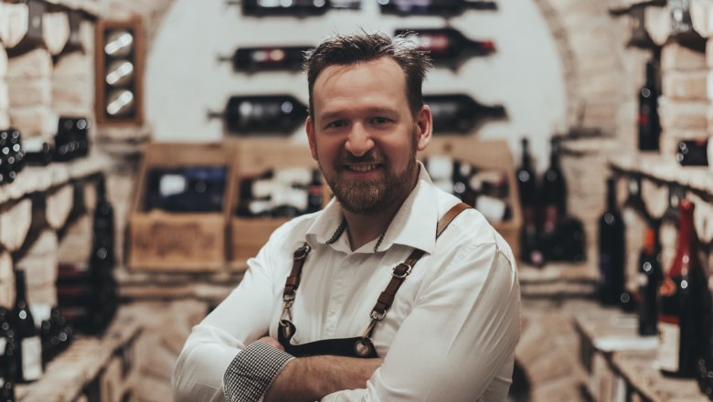 Wirt Christoph Hönig, © Niederösterreich Werbung/David Schreiber Ein Mann in einem Weinkeller mit Regalen voller Weinflaschen.