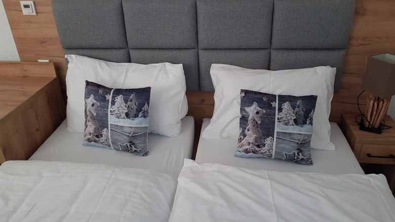 Doppelzimmer mit zwei Einzelbetten, grauem Kopfteil, graue Kissen und weißer Bettwäsche