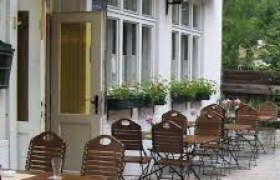 Außenbereich eines Gasthauses mit Holztischen und Stühlen, Blumenkästen an den Fenstern.