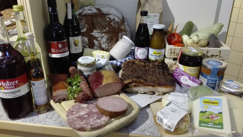 Verschiedene regionale Produkte wie Brot, Wurst, Käse und Getränke auf einem Tisch arrangiert.
