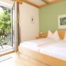 Helles Zimmer mit Doppelbett, gr&uuml;n gestrichener Wand und Balkon mit Bergblick.