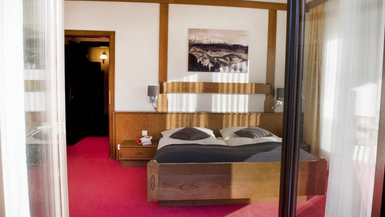 Ein gem&uuml;tliches Schlafzimmer mit einem Doppelbett, Holzm&ouml;beln und einem Bild an der Wand. Der Boden ist mit einem roten Teppich ausgelegt.