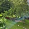 Ein gr&uuml;ner Garten mit B&auml;umen, einer Schaukel und einer Rutsche.