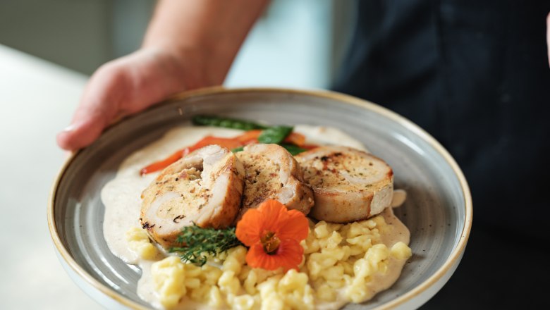 Ein Teller mit gefülltem Fleisch, Spätzle, Gemüse und einer Blume als Garnitur.