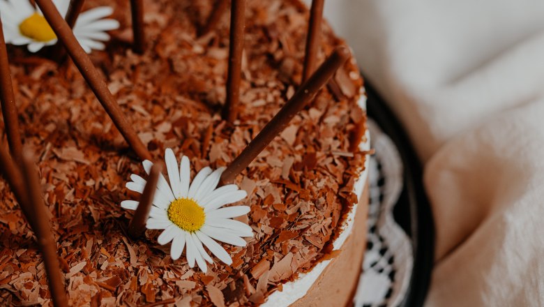 Schokoladentorte mit Schokostäbchen und Gänseblümchen dekoriert.