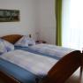 Doppelzimmer mit Holzbett, blau-wei&szlig; karierter Bettw&auml;sche, Bild an der Wand und gr&uuml;nem Vorhang.