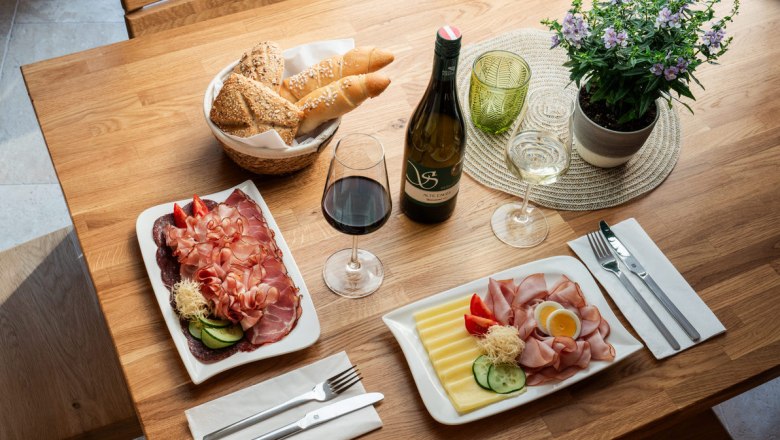 Ein Tisch mit regionalen K&ouml;stlichkeiten: Aufschnitt, K&auml;se, Brot, Rot- und Wei&szlig;wein.