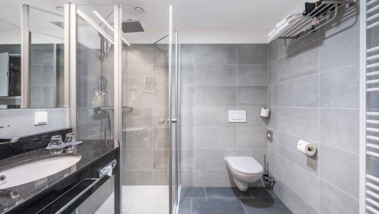 Modernes Badezimmer mit grauen Fliesen, Dusche, Waschbecken und WC.