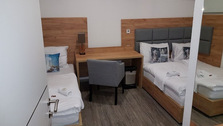 Dreibettzimmer mit zwei Einzelbetten, Schreibtisch und Stuhl.