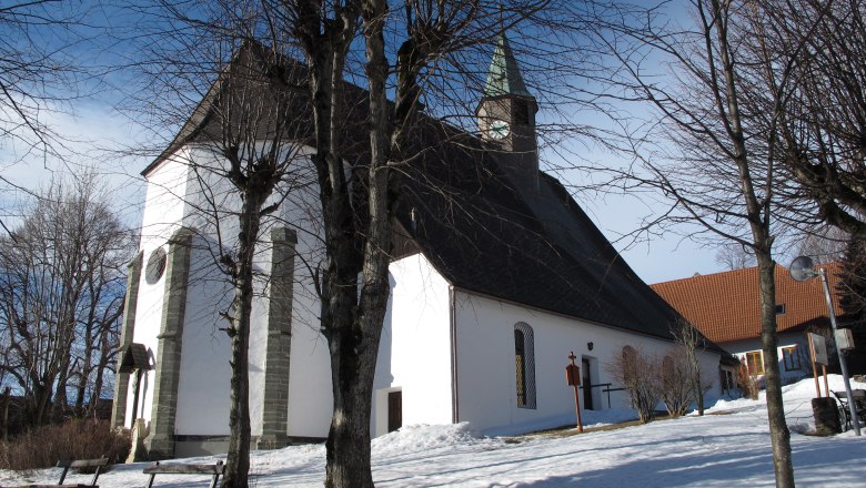 Pfarrkirche Maria Namen im Winter mit schneebedecktem Boden und kahlen Bäumen.