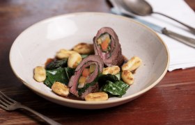 Roulade von der Rehschale mit Mangold und Wurzelgem&uuml;se, serviert mit Gnocchi auf einem Teller.