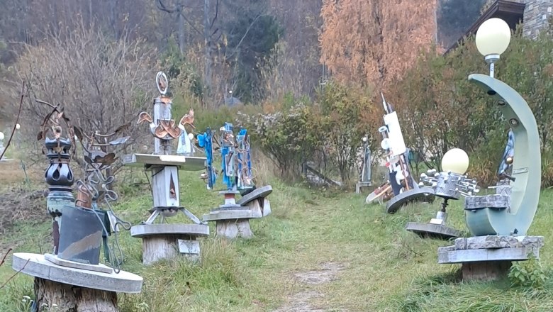 Ein Pfad im Skulpturenpark Semmering, ges&auml;umt von abstrakten Metallskulpturen auf Holzsockeln, umgeben von herbstlicher Vegetation.