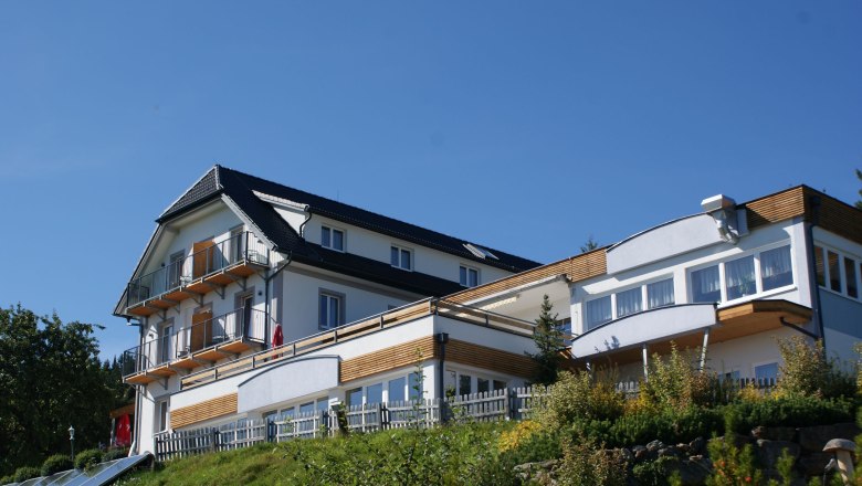 Ein modernes Hotelgebäude mit Balkonen und großen Fenstern auf einem Hügel unter blauem Himmel.