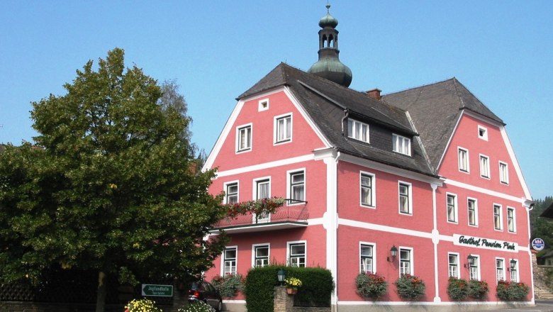 Ein altrosafarbenes zweist&ouml;ckiges Geb&auml;ude mit wei&szlig;en Fensterrahmen und grauem Dach.