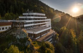 Ein Hotel auf einem H&uuml;gel bei Sonnenuntergang, umgeben von Wald.