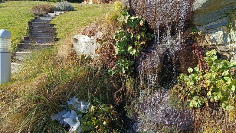 Kleiner Wasserfall in herbstlicher Landschaft mit Bäumen und blauem Himmel.