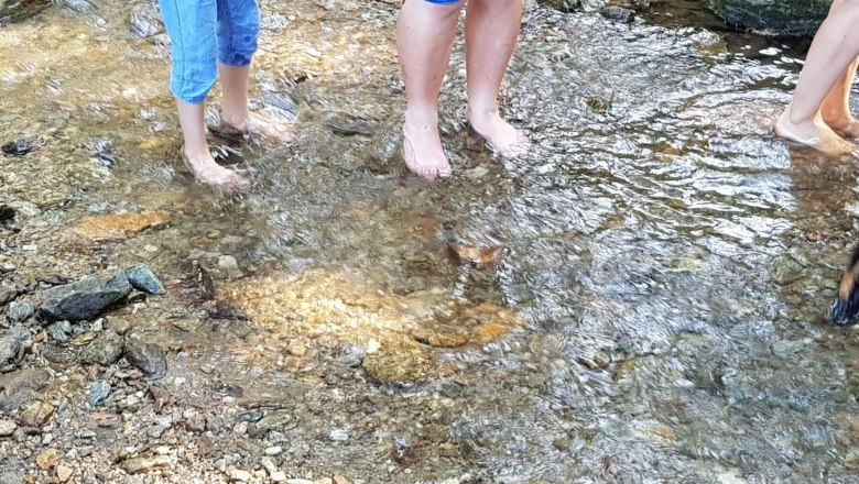 Menschen stehen barfu&szlig; in einem flachen Bach.