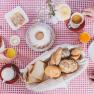 Fr&uuml;hst&uuml;ckstisch mit Br&ouml;tchen, Kuchen, Aufschnitt und Getr&auml;nken auf rot-wei&szlig; kariertem Tischtuch.
