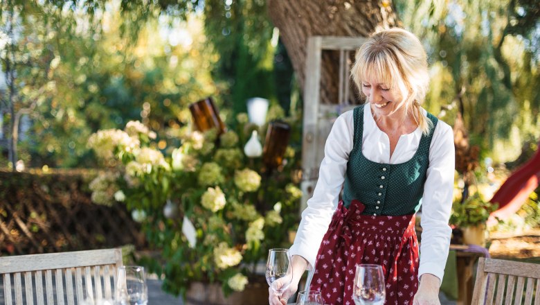 Frau in traditioneller Kleidung deckt einen Tisch im Freien.